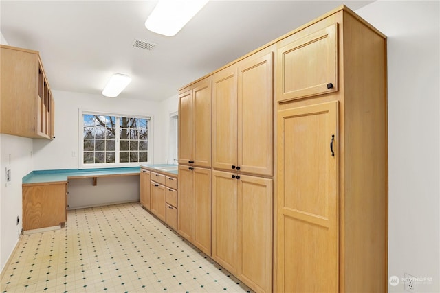 kitchen with light brown cabinetry, built in desk, and sink