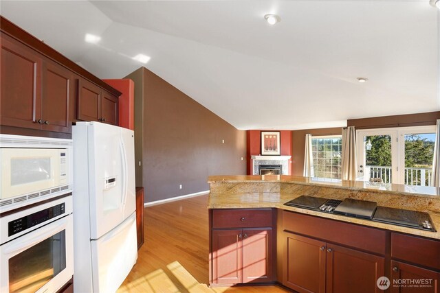 kitchen with lofted ceiling, light stone counters, white appliances, and light hardwood / wood-style floors