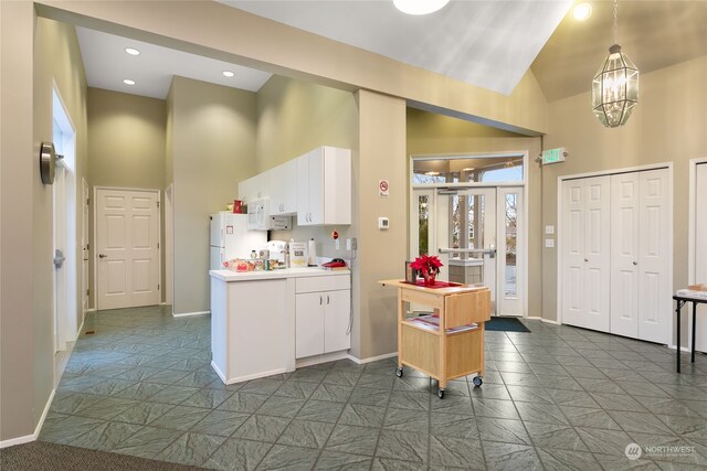 kitchen featuring white appliances, high vaulted ceiling, hanging light fixtures, white cabinetry, and a chandelier