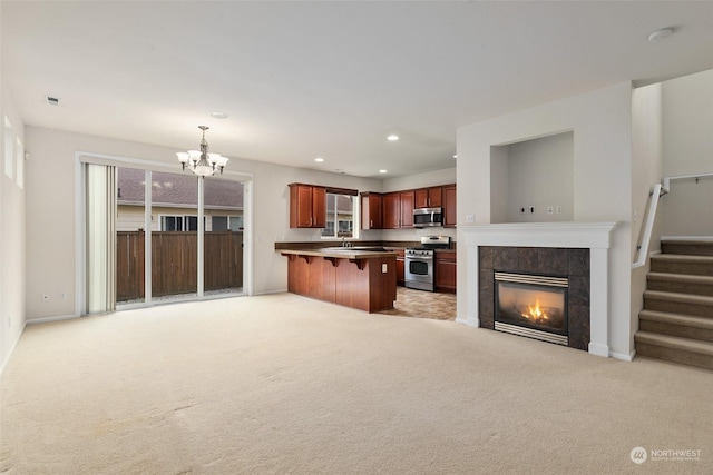 kitchen featuring a kitchen bar, appliances with stainless steel finishes, light carpet, a fireplace, and hanging light fixtures