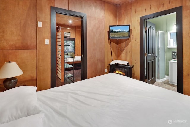 bedroom featuring ensuite bathroom, wood walls, and a wood stove