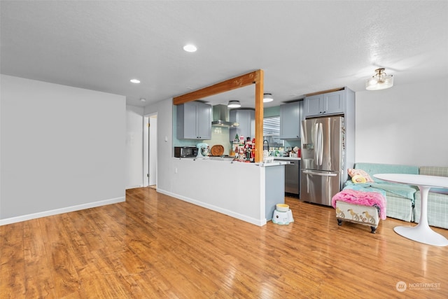 kitchen featuring stainless steel refrigerator with ice dispenser, light hardwood / wood-style flooring, wall chimney exhaust hood, gray cabinets, and kitchen peninsula