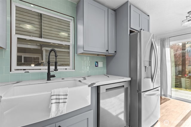 kitchen with gray cabinetry, decorative backsplash, a sink, wood finished floors, and stainless steel fridge