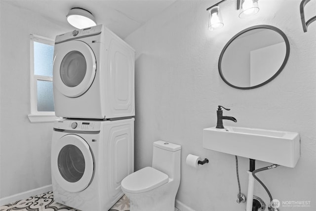 half bathroom featuring stacked washer and dryer, a sink, toilet, and baseboards