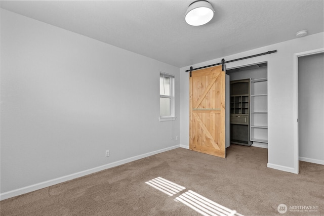 unfurnished bedroom featuring carpet floors, a barn door, a spacious closet, and baseboards
