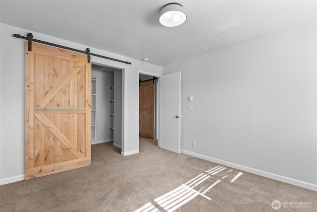 unfurnished bedroom with carpet, a barn door, and baseboards