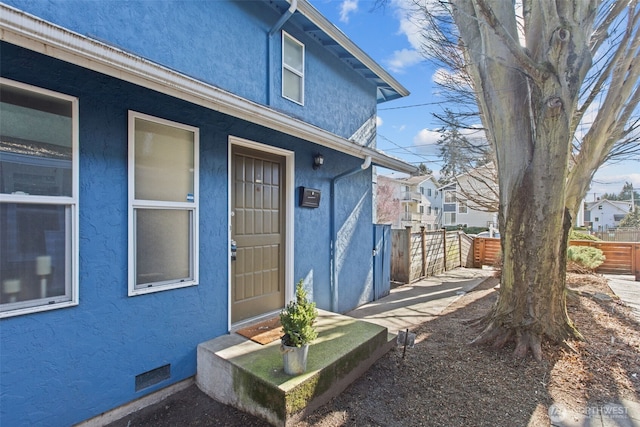 entrance to property featuring crawl space, visible vents, fence, and stucco siding
