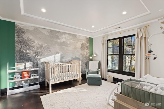 bedroom featuring a raised ceiling, wood-type flooring, a crib, and ornamental molding