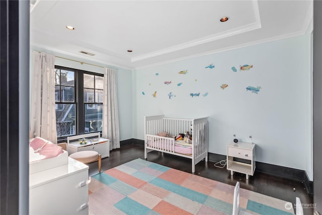 bedroom featuring a raised ceiling, ornamental molding, dark wood-type flooring, and a nursery area