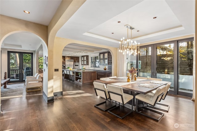 dining area with a notable chandelier, dark hardwood / wood-style floors, a raised ceiling, and french doors