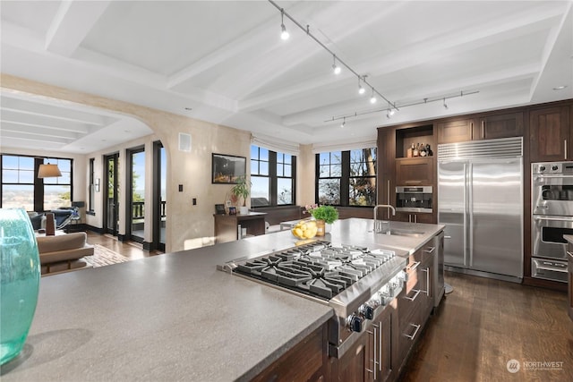 kitchen featuring dark hardwood / wood-style flooring, dark brown cabinets, stainless steel appliances, sink, and beamed ceiling