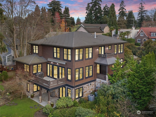 back house at dusk featuring a yard, central AC, and a balcony