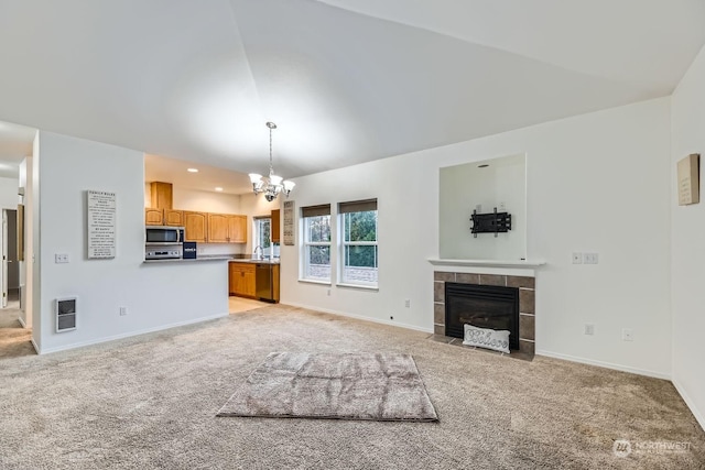 unfurnished living room featuring a tile fireplace, light carpet, a chandelier, and sink