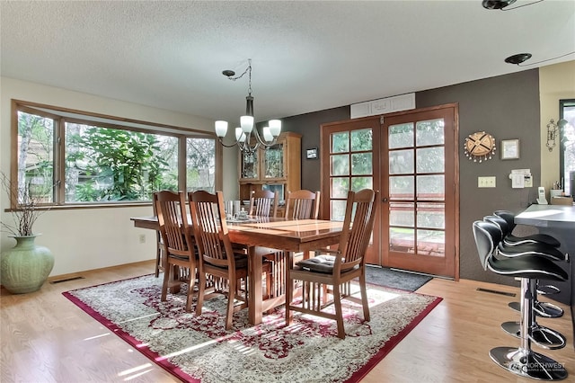 dining area with french doors, light wood-type flooring, a textured ceiling, and an inviting chandelier