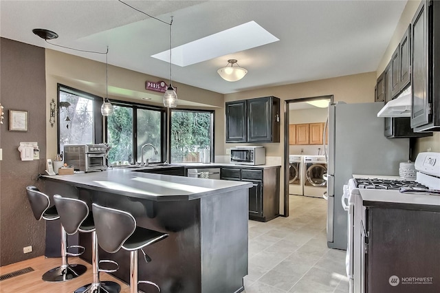 kitchen with washing machine and clothes dryer, a skylight, kitchen peninsula, decorative light fixtures, and white range with gas cooktop