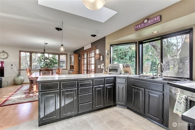 kitchen featuring sink, light hardwood / wood-style flooring, stainless steel dishwasher, decorative light fixtures, and kitchen peninsula