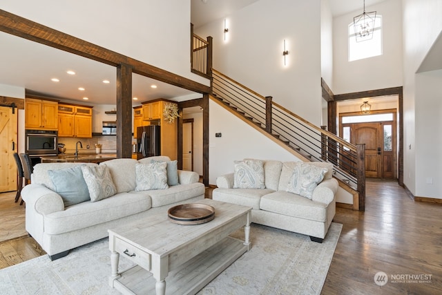 living room featuring light wood-type flooring, sink, a high ceiling, and an inviting chandelier