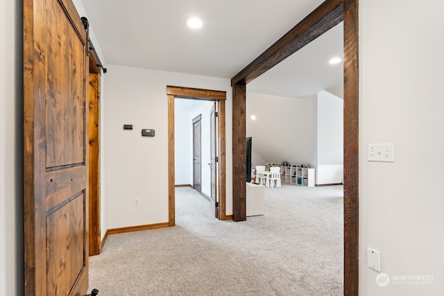 hallway with beamed ceiling, a barn door, and light colored carpet