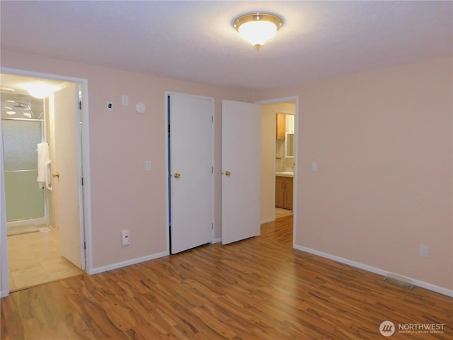 unfurnished bedroom with ensuite bathroom and light wood-type flooring