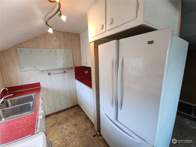 kitchen with wood walls, white fridge, lofted ceiling, and sink