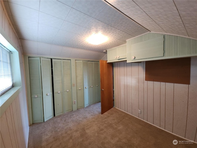 unfurnished bedroom featuring lofted ceiling, multiple closets, light carpet, and wood walls