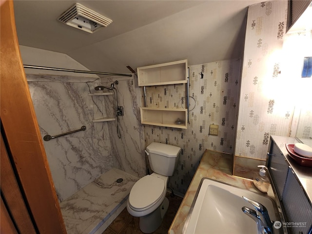 bathroom with a tile shower, vanity, toilet, and lofted ceiling