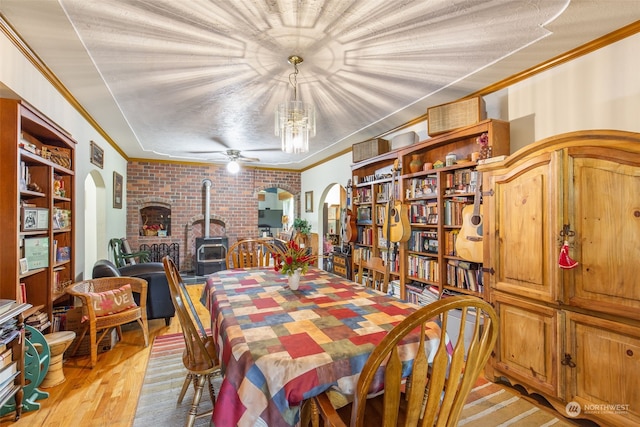 dining area featuring crown molding, light hardwood / wood-style floors, ceiling fan, and a wood stove