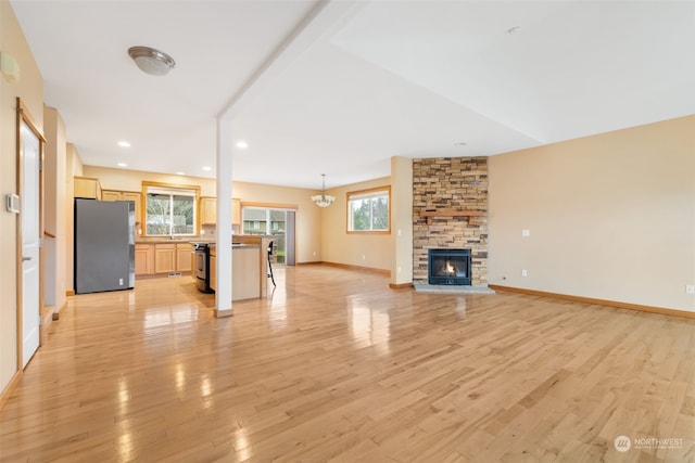 unfurnished living room with a notable chandelier, light hardwood / wood-style flooring, and a stone fireplace