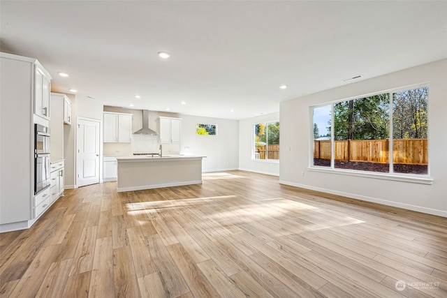 kitchen with recessed lighting, light countertops, light wood-style floors, wall chimney exhaust hood, and open floor plan