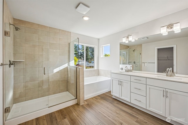 full bathroom featuring a garden tub, a stall shower, a sink, wood finished floors, and double vanity