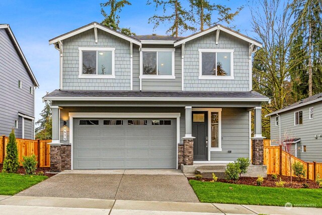 craftsman-style home with a garage, stone siding, driveway, and fence