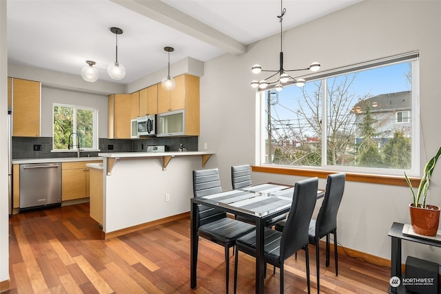 kitchen with dark wood-type flooring, stainless steel appliances, backsplash, decorative light fixtures, and light brown cabinetry