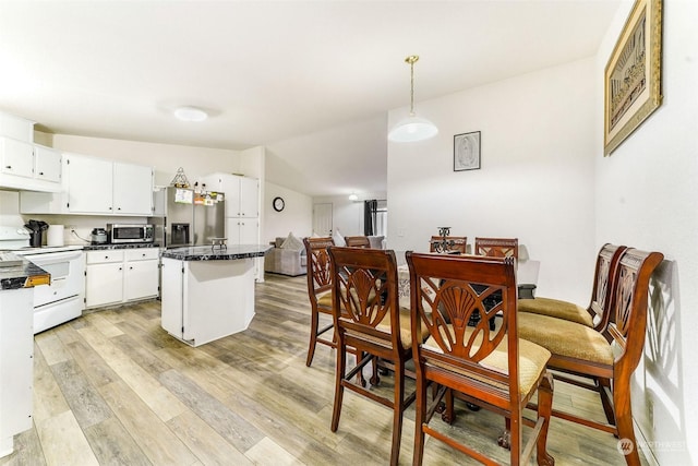 kitchen with white cabinets, vaulted ceiling, light wood-type flooring, decorative light fixtures, and stainless steel appliances