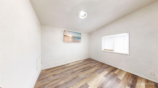 empty room featuring wood-type flooring and vaulted ceiling