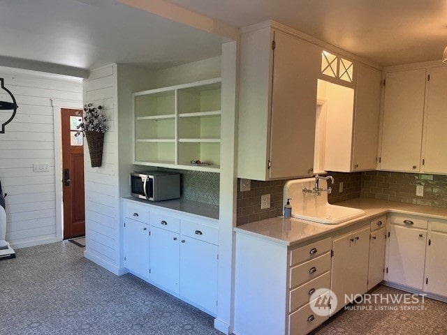 kitchen featuring white cabinets, wood walls, sink, and tasteful backsplash