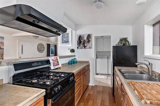 kitchen with extractor fan, dark wood-type flooring, sink, washer and dryer, and black appliances