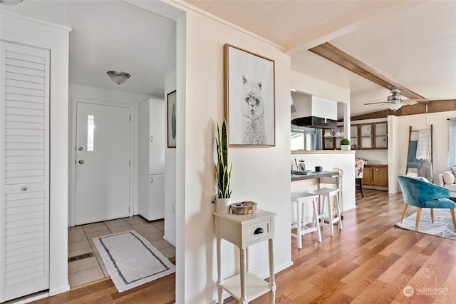 interior space with beam ceiling, ceiling fan, and light wood-type flooring