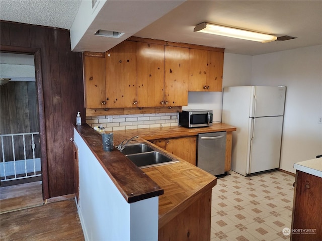 kitchen with appliances with stainless steel finishes, tasteful backsplash, a textured ceiling, sink, and butcher block counters