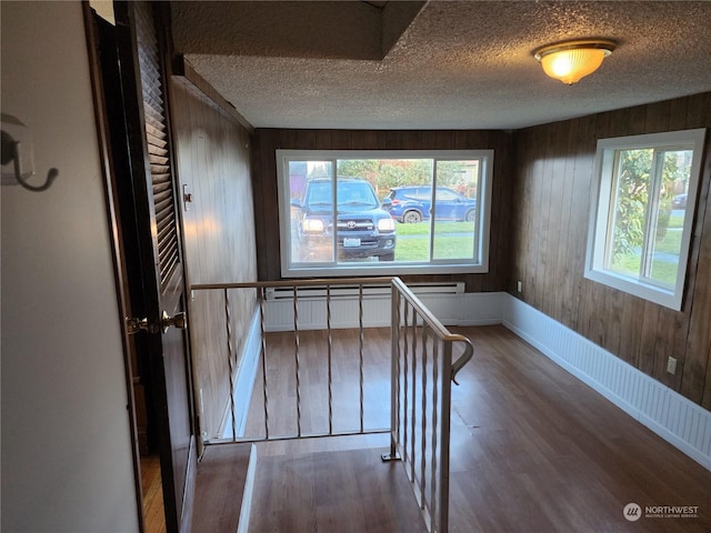 unfurnished room featuring wooden walls, a baseboard radiator, wood-type flooring, and a textured ceiling