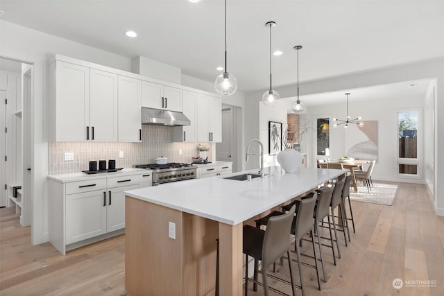 kitchen with white cabinetry, hanging light fixtures, sink, a center island with sink, and stainless steel range