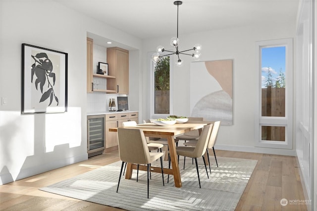 dining space with light wood-style flooring, wine cooler, a chandelier, and baseboards