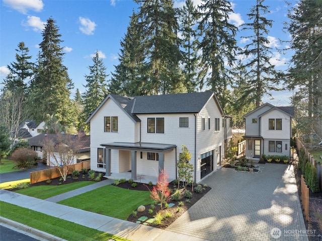 modern inspired farmhouse featuring decorative driveway, covered porch, a front yard, fence, and a garage