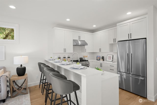 kitchen featuring a breakfast bar, white cabinetry, light hardwood / wood-style floors, kitchen peninsula, and stainless steel appliances