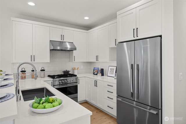 kitchen with tasteful backsplash, premium appliances, sink, light hardwood / wood-style flooring, and white cabinets