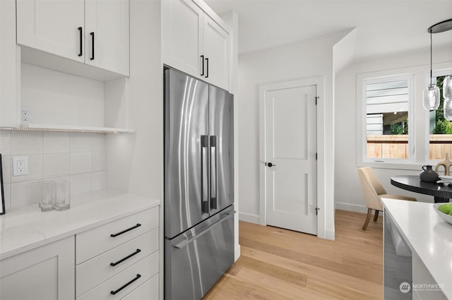 kitchen with white cabinets, hanging light fixtures, stainless steel fridge, tasteful backsplash, and light hardwood / wood-style floors