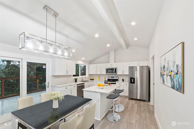 kitchen with beam ceiling, white cabinetry, stainless steel appliances, a kitchen island, and light wood-type flooring