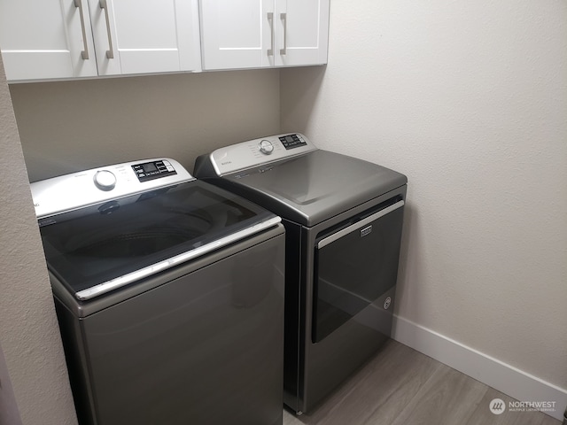 laundry area featuring washer and dryer, light wood-type flooring, and cabinets