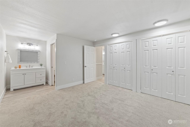 unfurnished bedroom featuring two closets, connected bathroom, light colored carpet, and sink