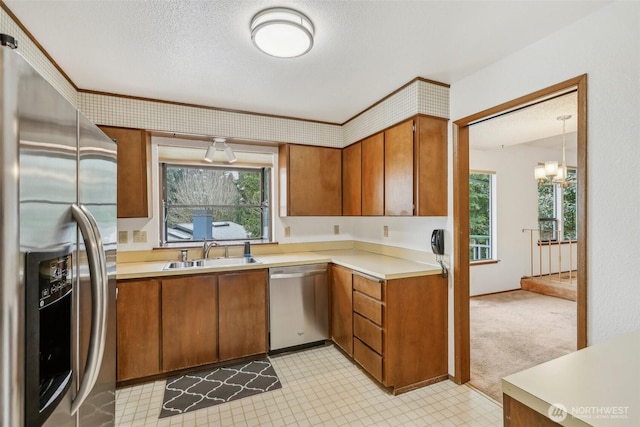 kitchen featuring light countertops, stainless steel appliances, brown cabinetry, a textured ceiling, and a sink