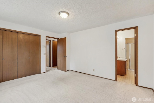 unfurnished bedroom with a textured ceiling, ensuite bath, a closet, and light carpet